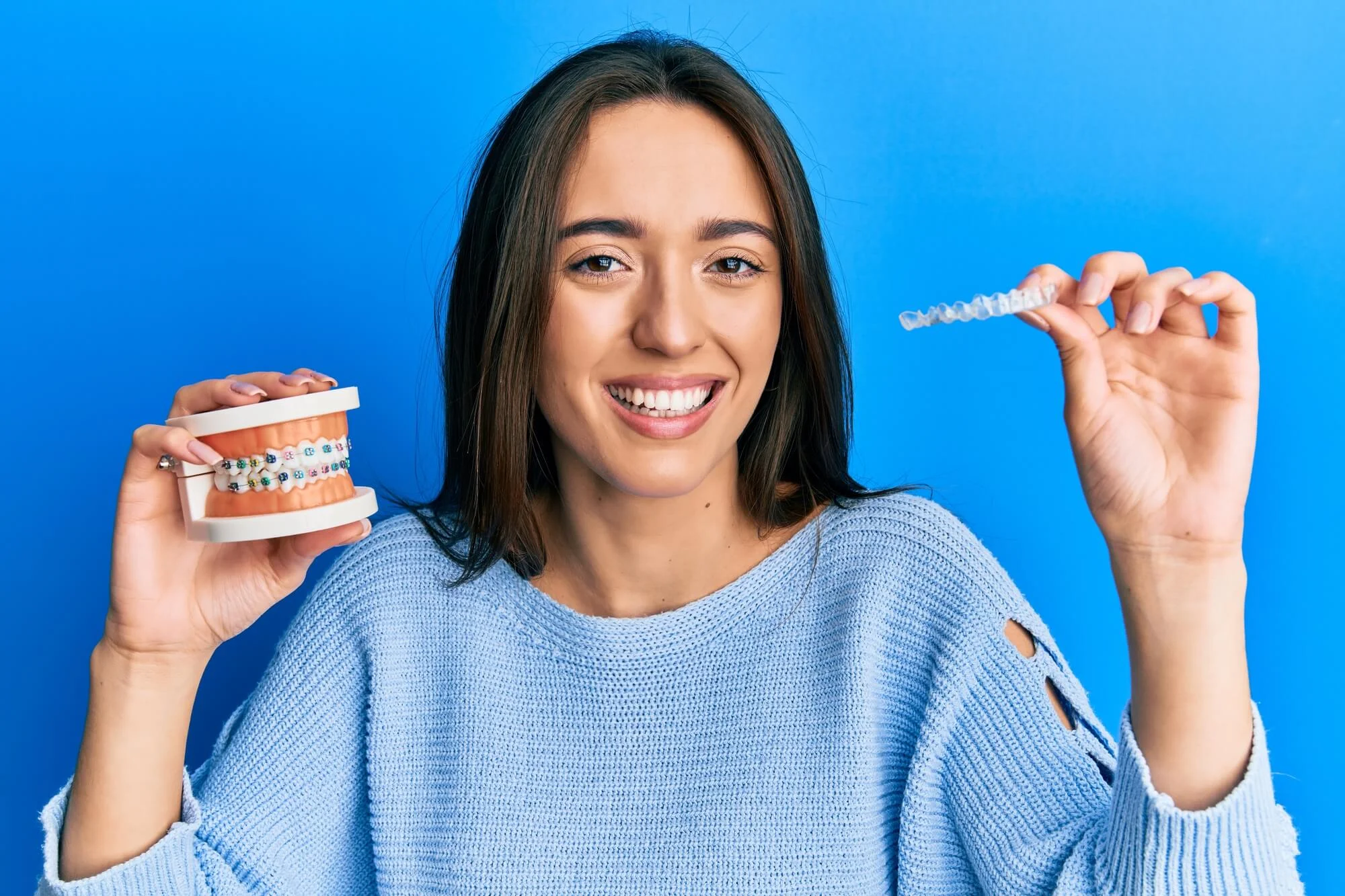 Young-smling-woman-holding-plastic-teeth-with-braces