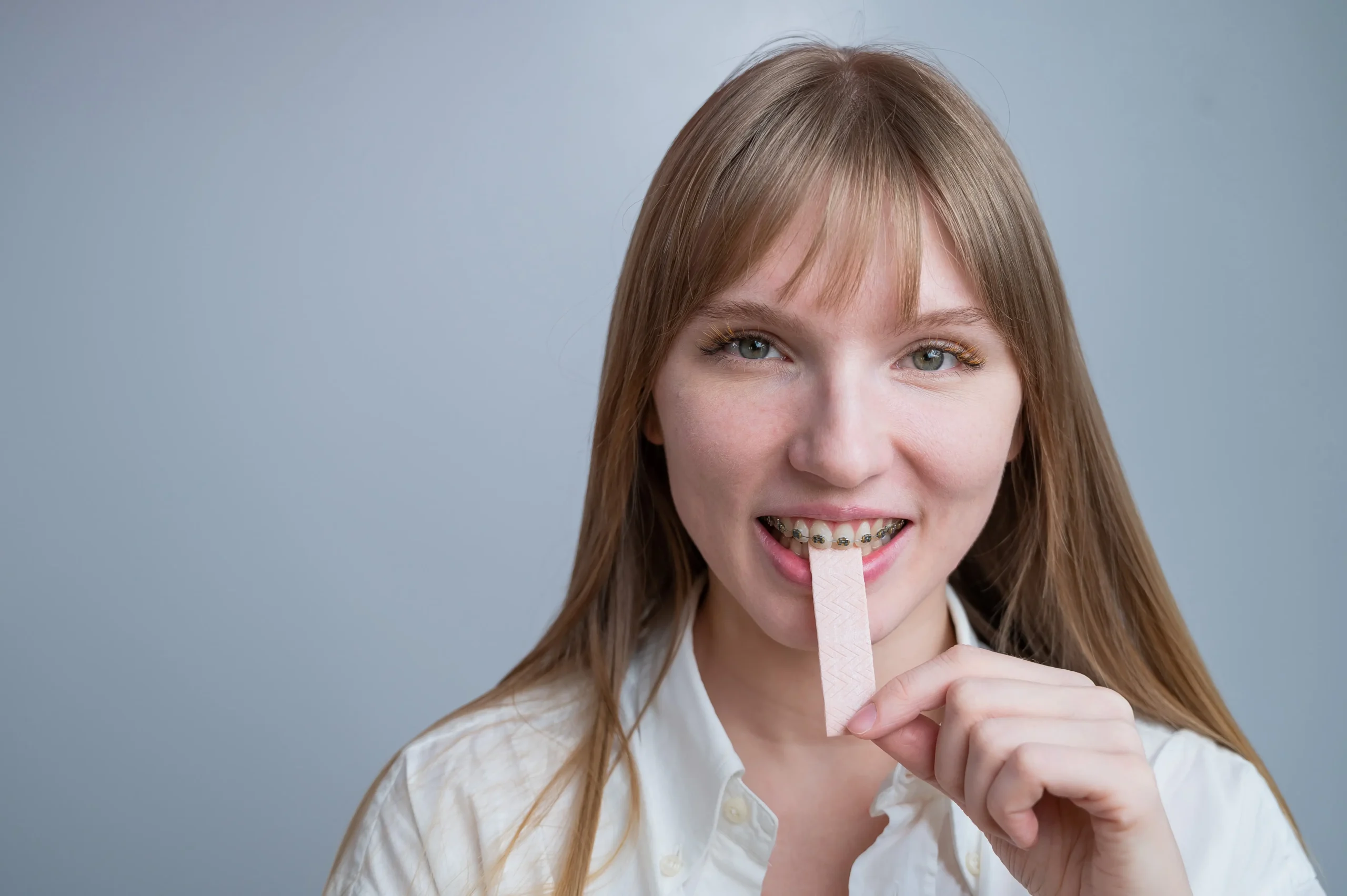 Woman wearing braces holding a piece of chewing gum to her mouth.