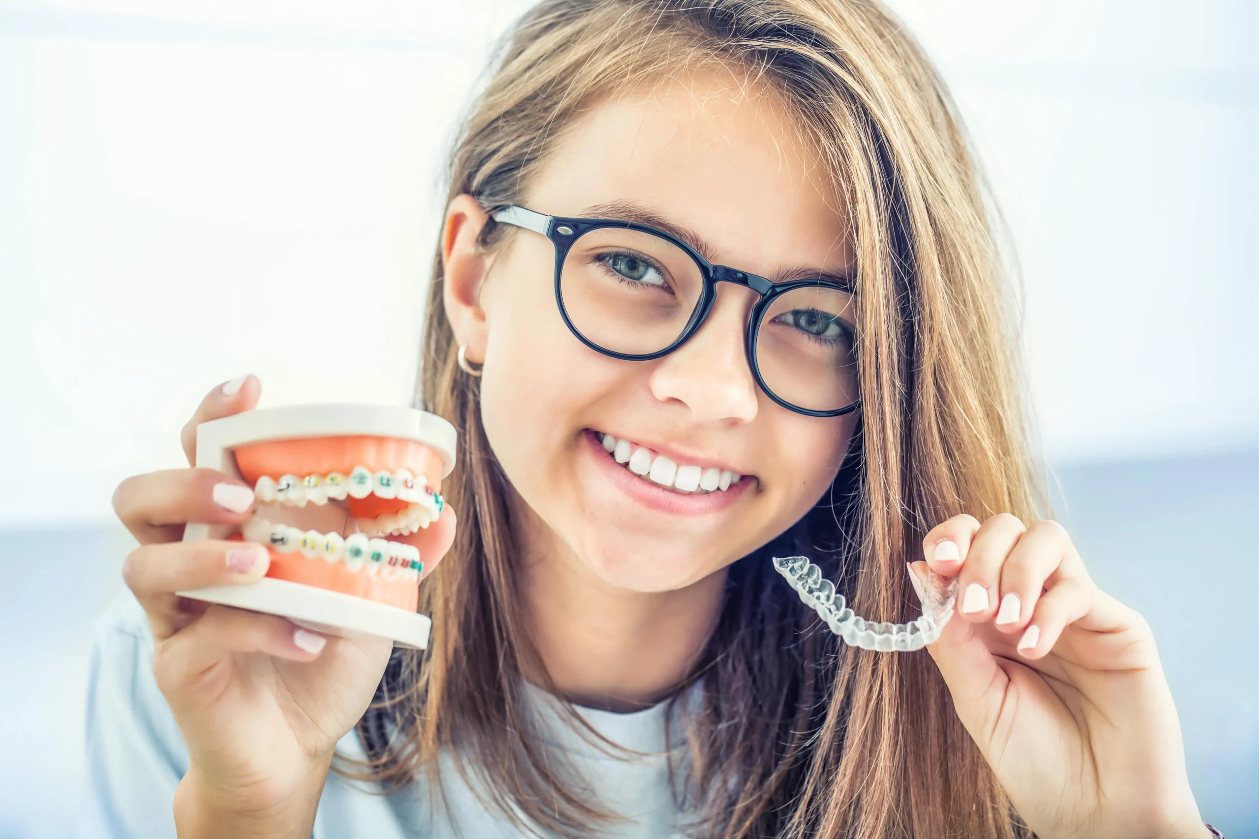A young woman holding a pair of Invisalign aligners and braces